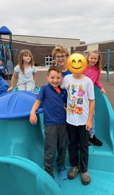 A group of young students posing together on a blue playground structure.