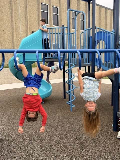 Elementary students hanging upside down and playing on playground climbing equipment.