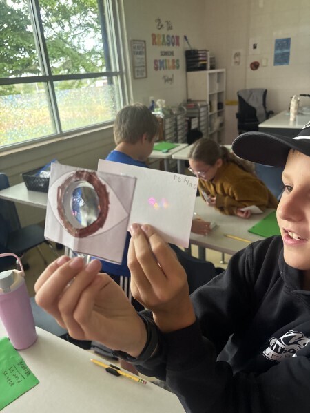 A student tests a paper eye model with a lens to project light onto a retina card during a classroom science lesson.