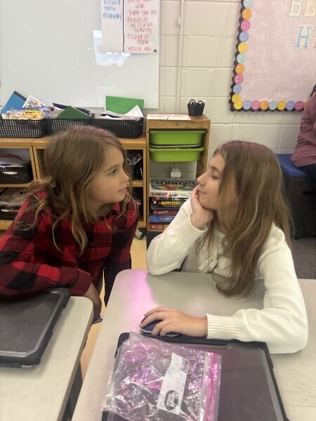 Two students sit together at classroom desks during a peer discussion activity.