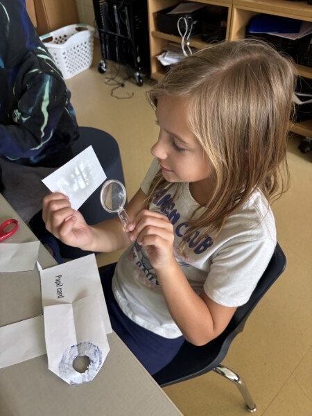A student uses a magnifying glass and paper model to study how human eyes focus light.