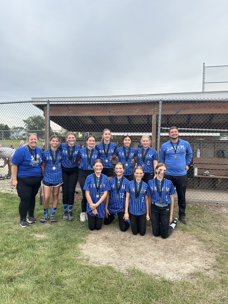 Salem youth softball team members and their coaches smiling and standing together on the dirt field wearing medals.