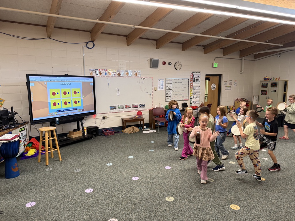 Class of young students playing hand tambourines and moving around the room during music instruction.