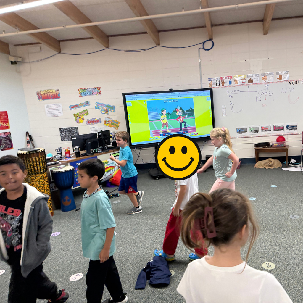 Elementary students walking in a circle during a music classroom activity while following an interactive video screen.