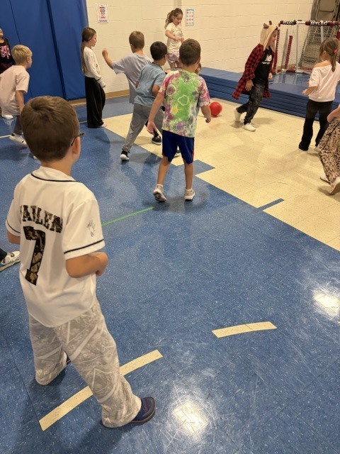 Children actively playing a gaga ball game on the gymnasium court during gym class.