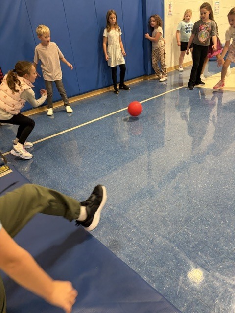 Students playing gaga ball on the gym floor as a red ball rolls across the court.