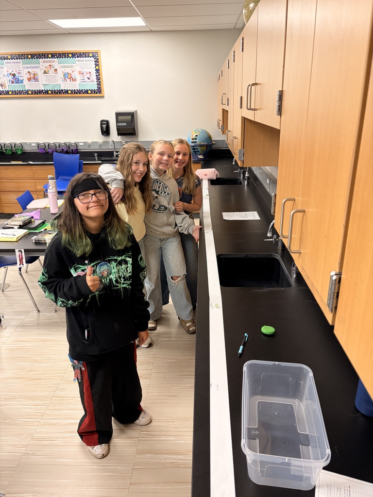 Four students posing near a paper measurement strip running along a lab counter in science class.