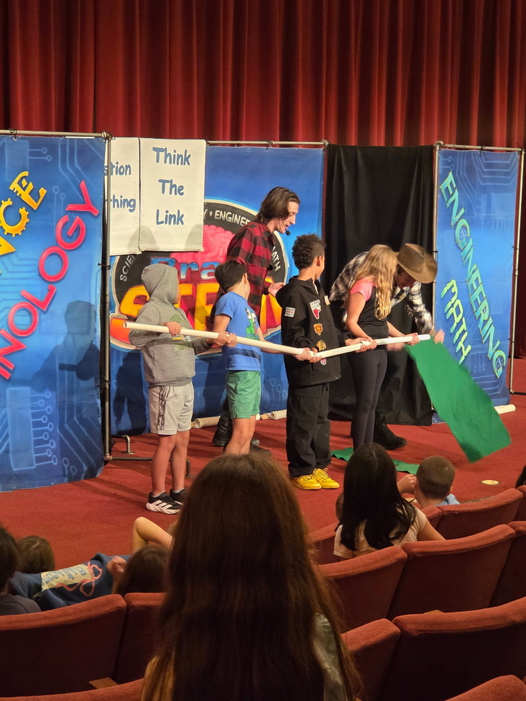 Students participating in an interactive STEM demonstration on stage during a school assembly.