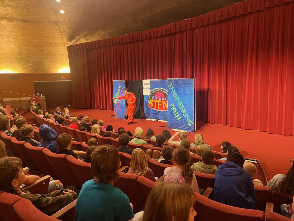 Presenters speaking to an auditorium filled with students during a STEM assembly.