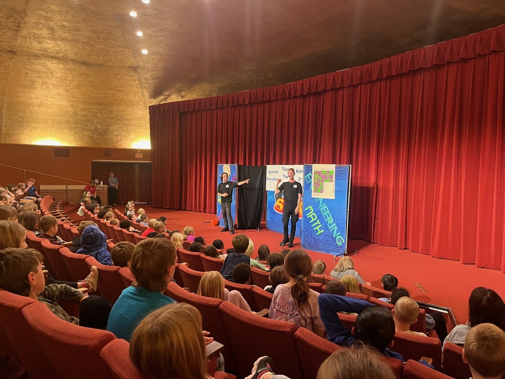 An audience of students watching a STEM presenter on stage in a school auditorium.
