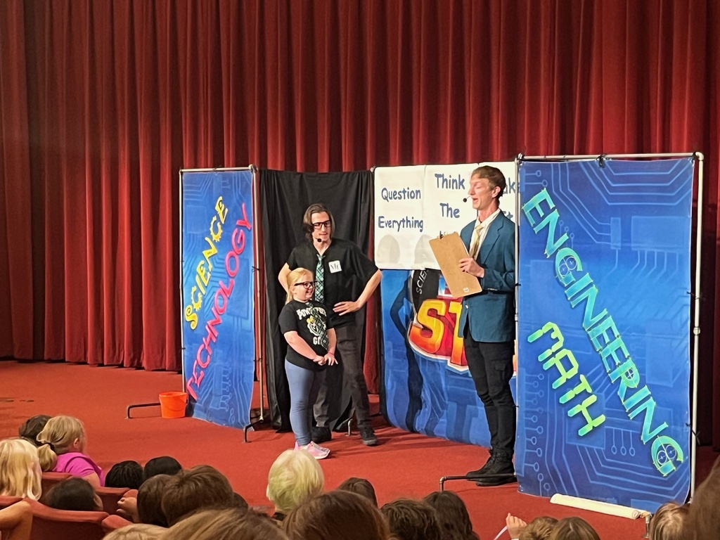 A student volunteer on stage with presenters during a STEM school presentation.