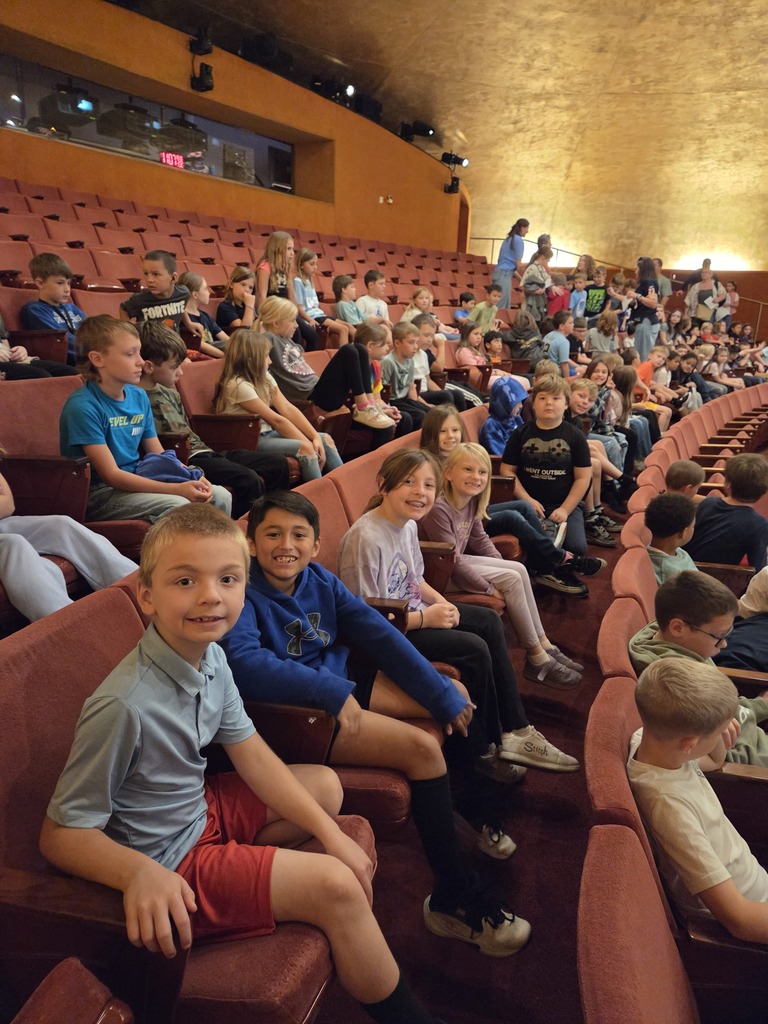 Students sitting in auditorium seating during a school assembly performance.