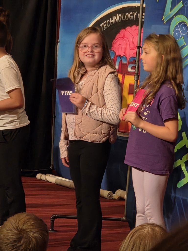 Two student volunteers standing on stage holding cards during a STEM presentation.