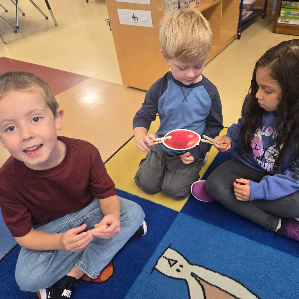 Three young students sitting on a colorful carpet working together using clothespins and paper cutouts during a learning activity.