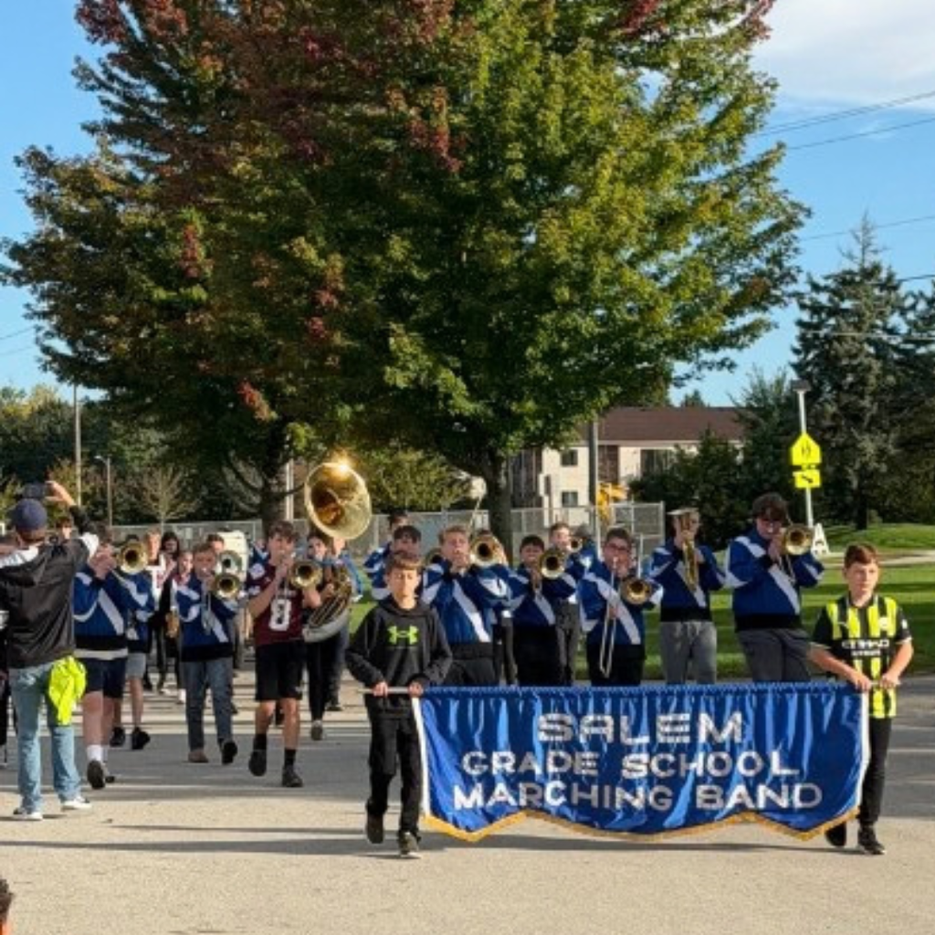 Two students holding a Salem Grade School Marching Band banner leading a band down the street.