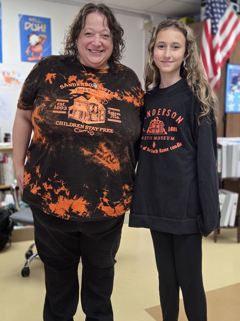 A smiling teacher and student pose together in a classroom, both wearing matching Halloween-themed Sanderson Sisters shirts.
