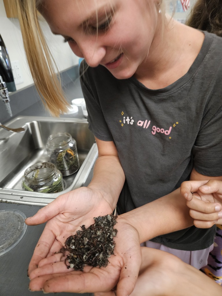A smiling student holding a handful of rich soil compost during a hands-on science classroom lesson.