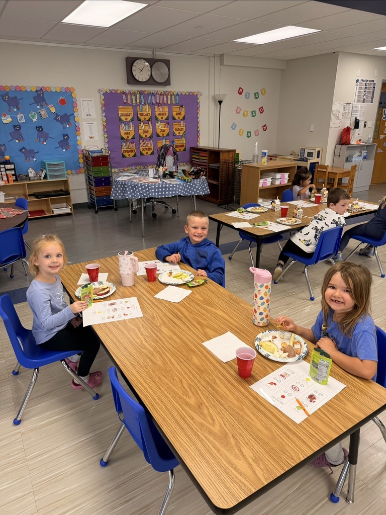 Young students smiling at a wooden classroom table while eating snacks during a tasting activity.