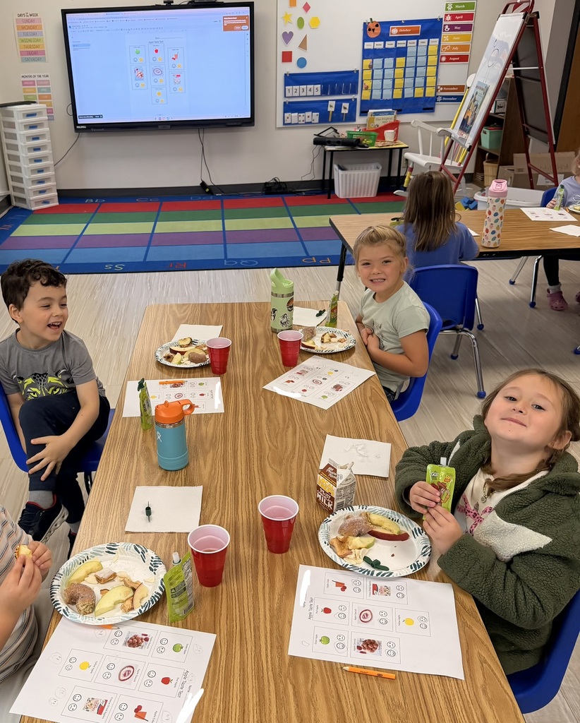 Children seated around a table in a bright classroom with apple snacks and activity worksheets.