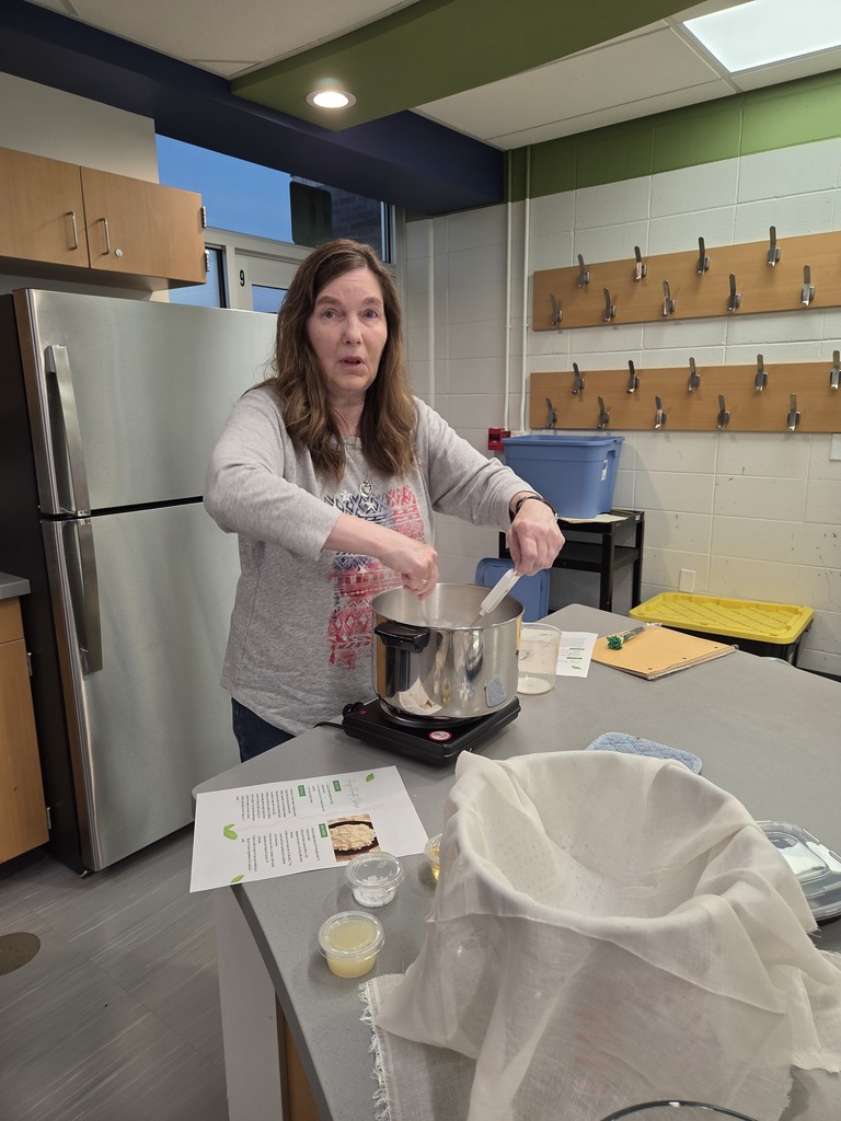 An instructor stirring ingredients in a stainless steel pot on a hot plate next to cheesecloth lined bowls.