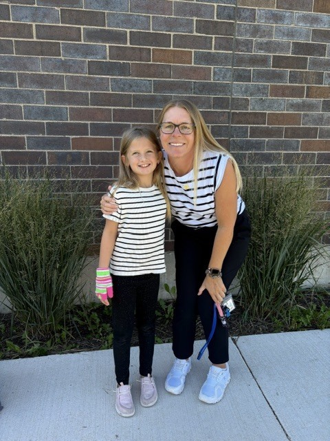 A teacher and young female student posing together in matching black-and-white striped shirts outdoors