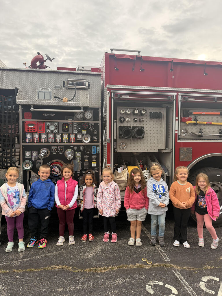 Nine young students standing in a line in front of an open Salem Lakes Fire Rescue fire truck during a fire safety presentation.