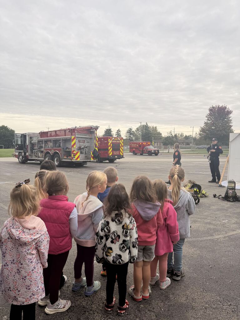 Young students outside in a group watching the fire fighters with an ambulance and firetruck in the background