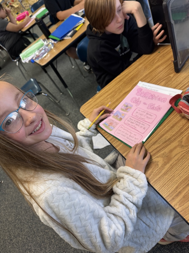 A student wearing glasses smiling next to her social studies poster detailing facts about Sumerian city-states.