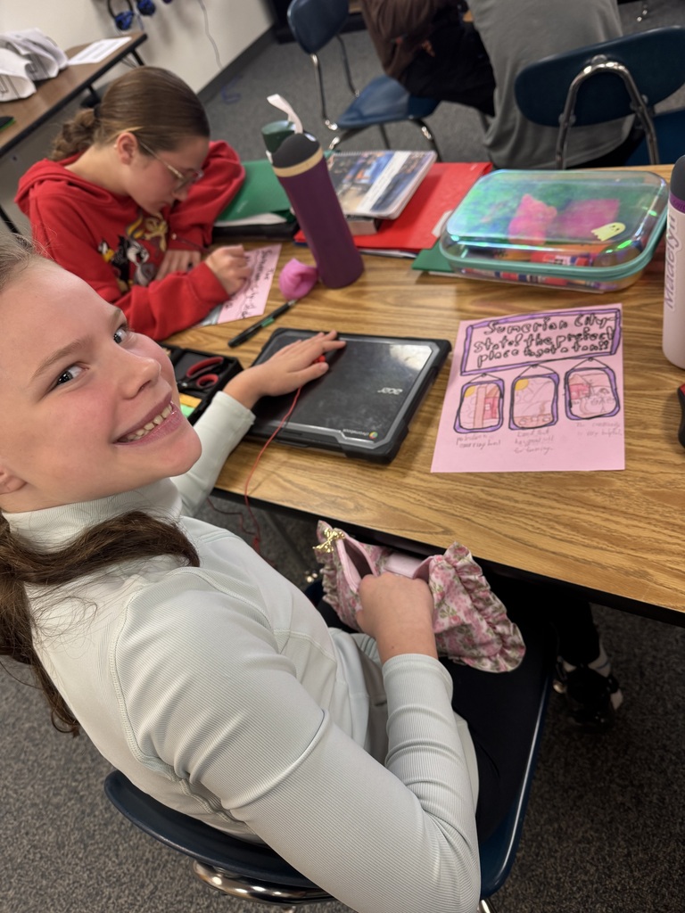 A smiling student at her desk displaying her completed pink poster project on Sumerian city-states.