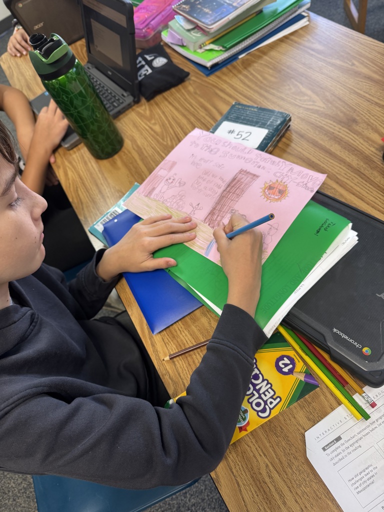 A student using colored pencils at a classroom desk to create a promotional poster about Sumerian city-states.