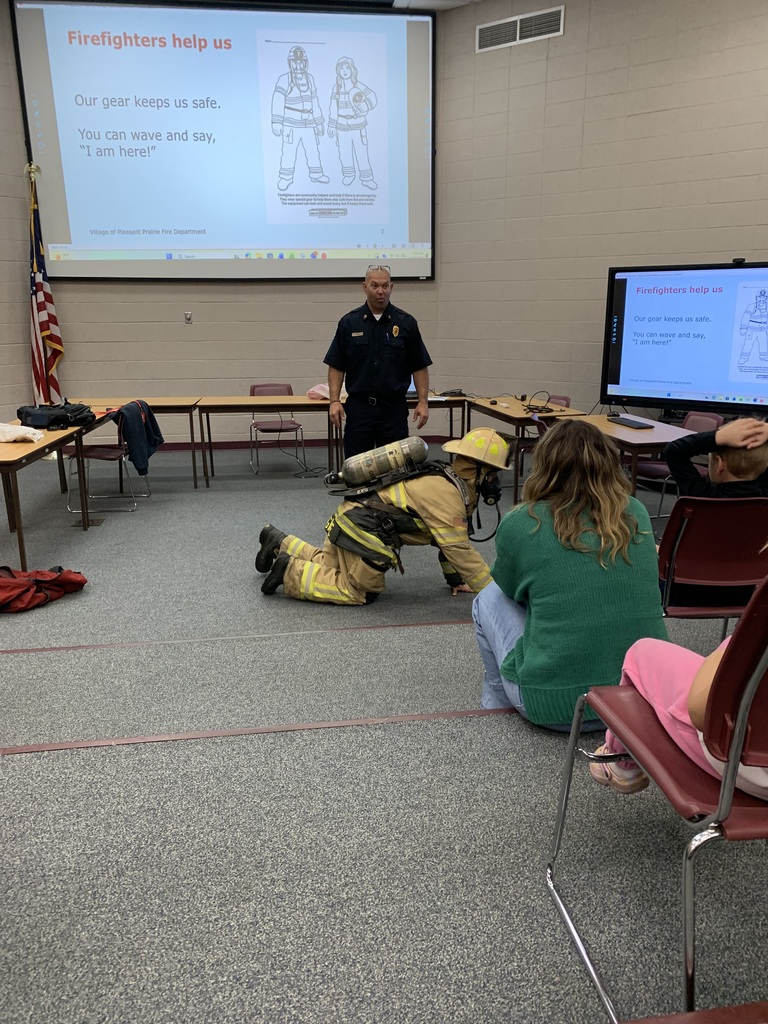 A firefighter in full gear crawls on the floor to demonstrate safety techniques during a school fire safety presentation.