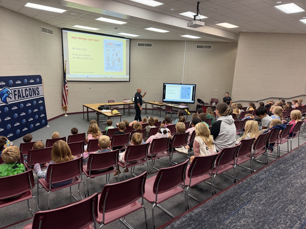 Students seated in an auditorium listen to a fire safety presentation titled "Hot things can hurt".