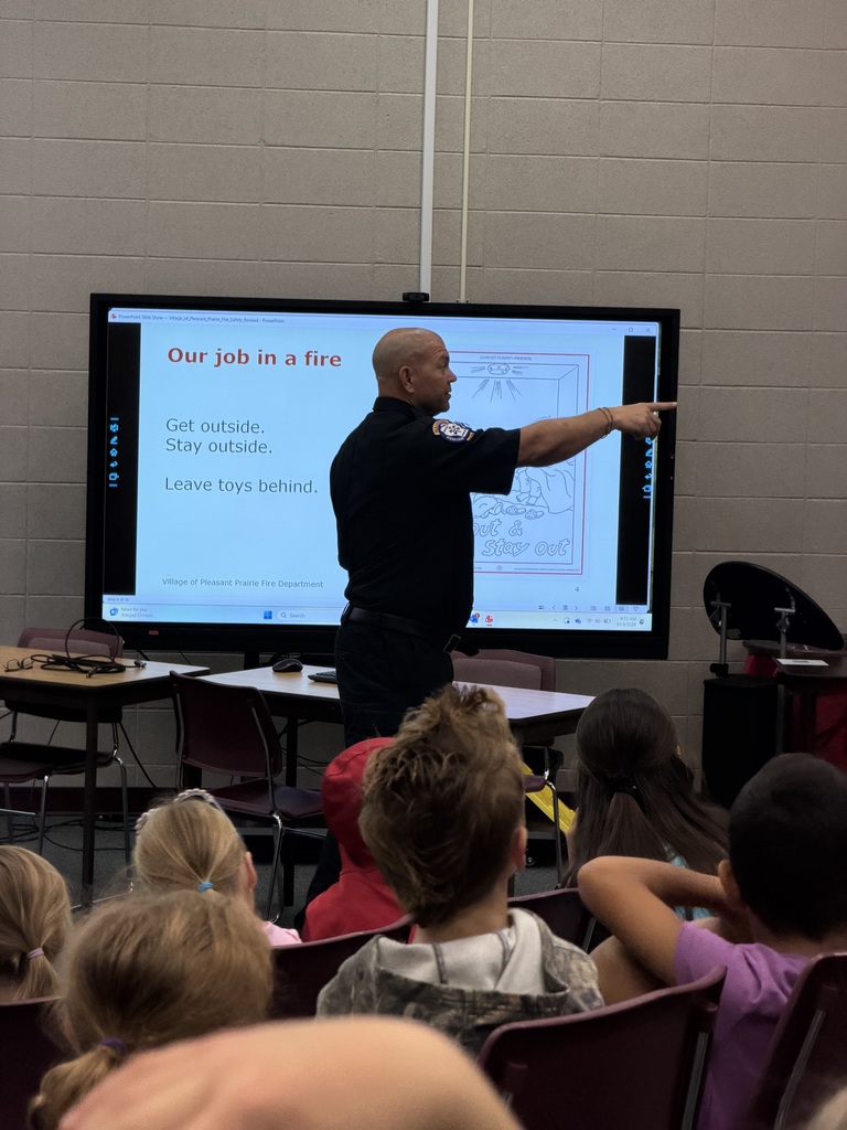 A fire official points to a display screen titled "Our job in a fire" while teaching students fire safety rules