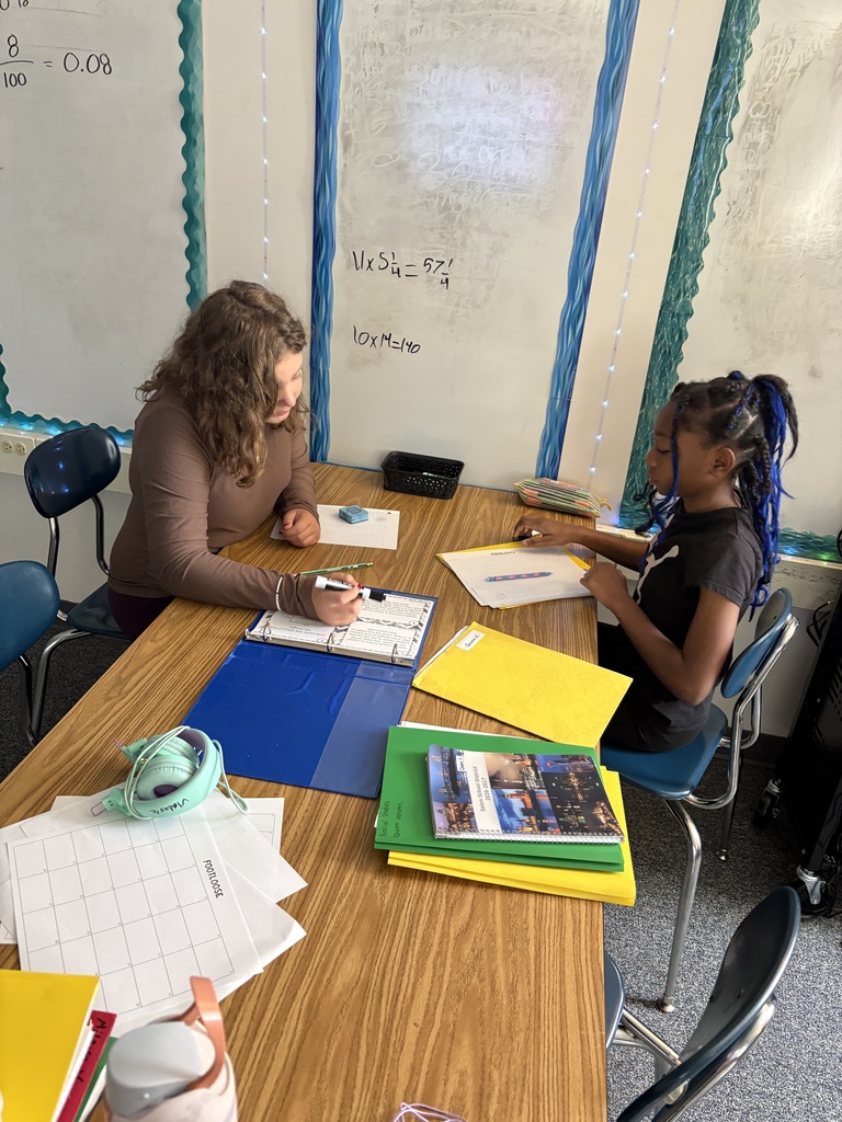 2 middle school students working together at a table that has many class materials on it.