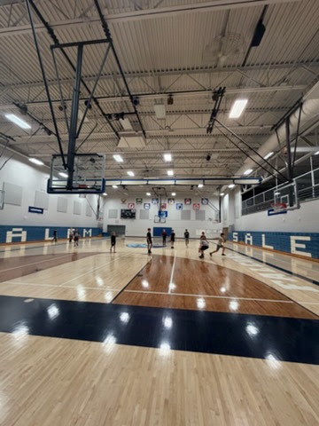 Wide view of students playing on a basketball court inside a spacious school gymnasium.