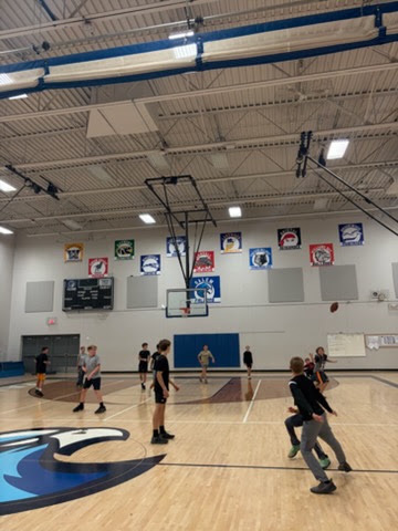 Students running across the gymnasium floor during an active indoor football game in open gym.
