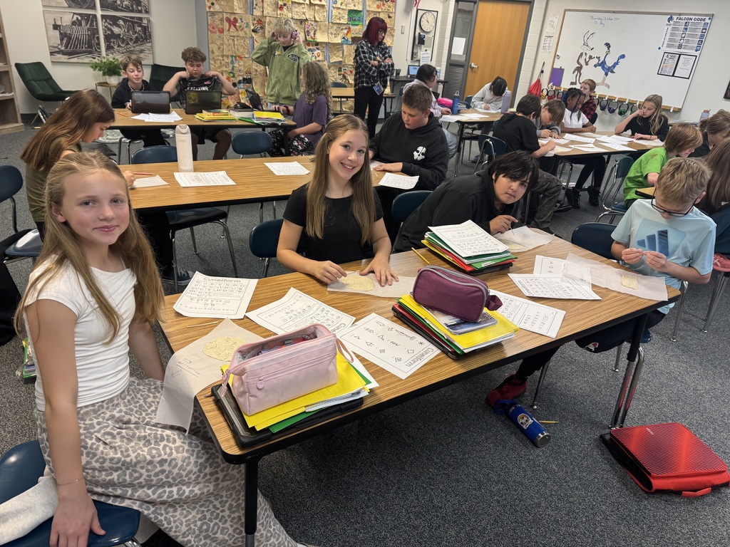 Classroom view of students working at desks on cuneiform clay projects with worksheets and materials spread out.