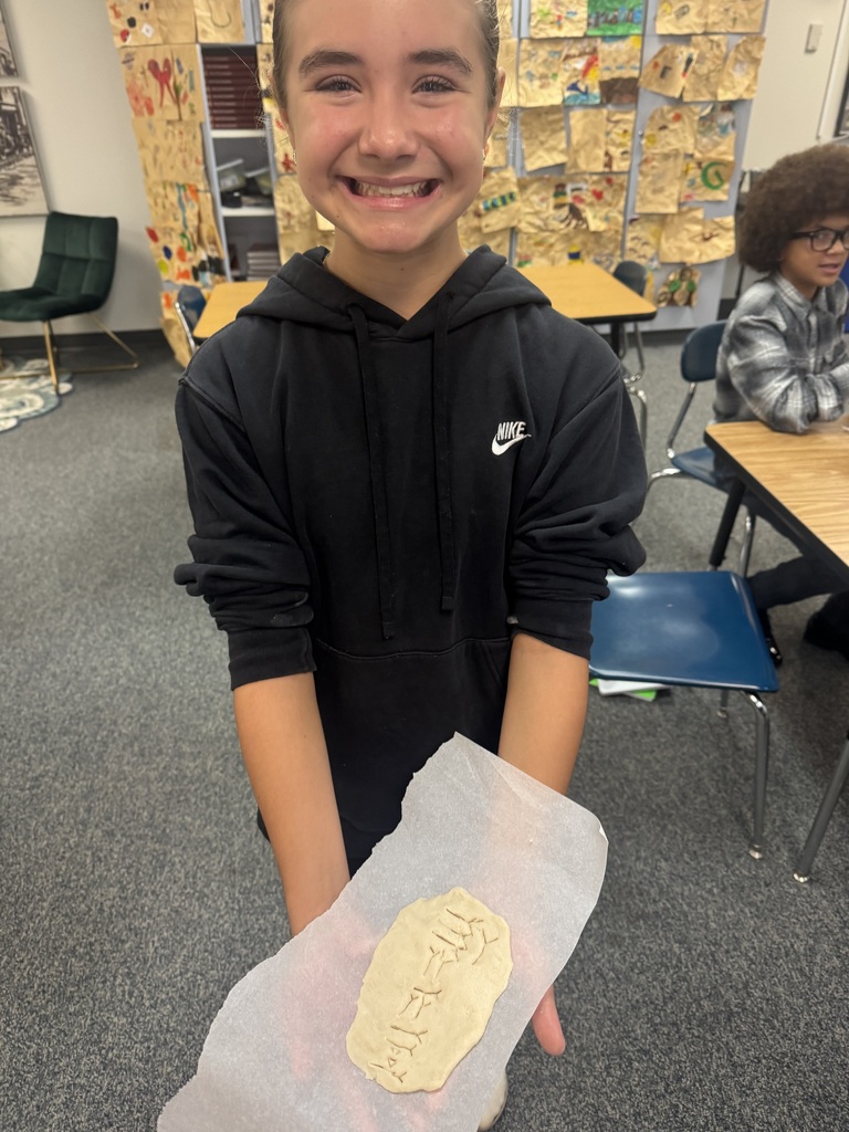 A smiling student holding a piece of dough inscribed with cuneiform symbols during a classroom lesson