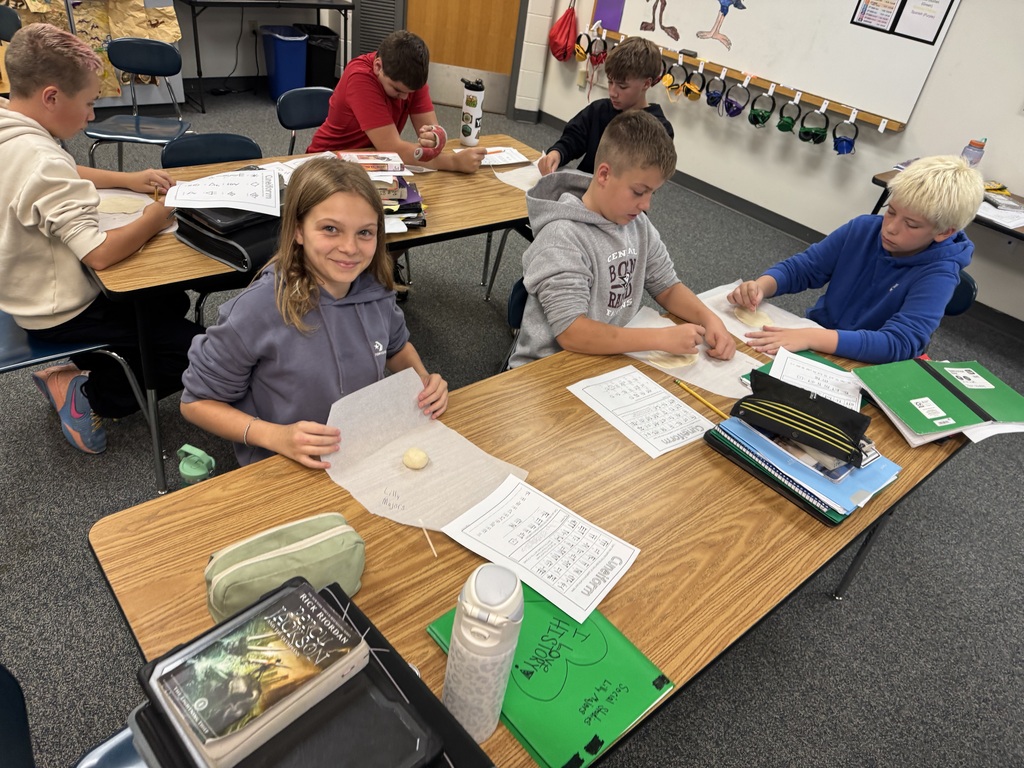 Students at classroom desks using tools and reference sheets to press cuneiform writing into clay.