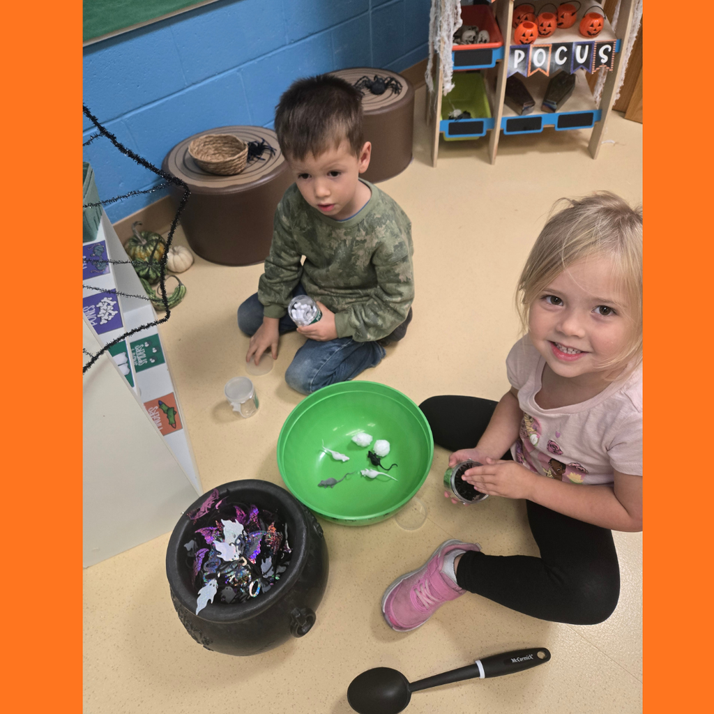 Two young elementary students sitting on the floor surrounded by Halloween-themed sensory toys, plastic mice, and a mini cauldron.