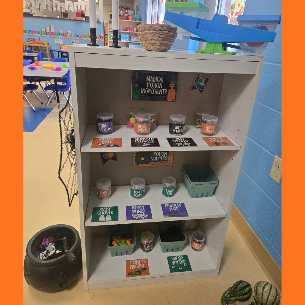 A classroom bookcase stocked with labeled jars for a Halloween "Magical Potion Ingredients" activity next to a toy cauldron.