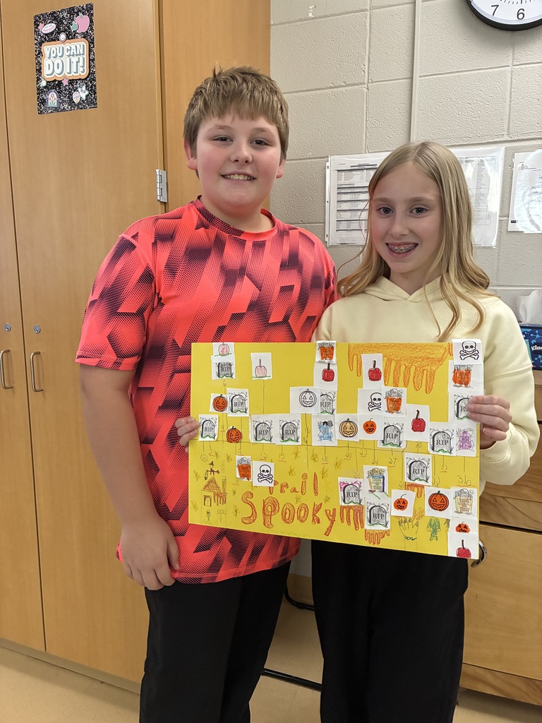 Two smiling students holding a yellow Halloween math poster titled "Spooky Trail" decorated with gravestone graphs and pumpkins.