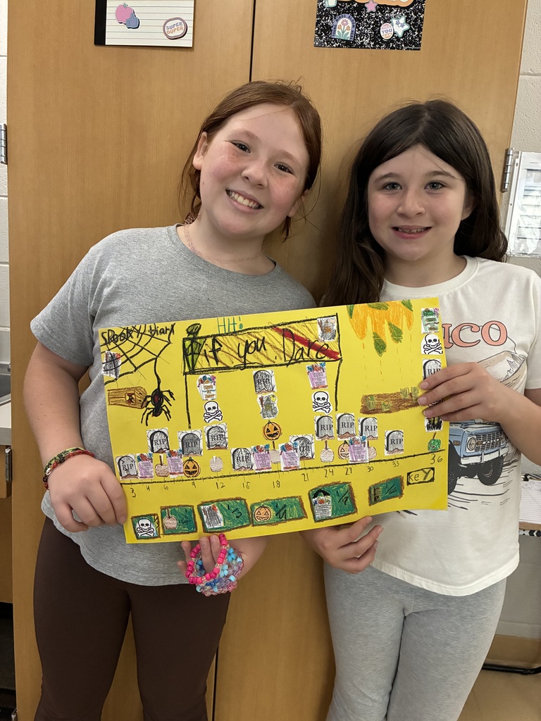 Two smiling students presenting a yellow Halloween math poster with a number line graph, gravestones, spiders, and pumpkins