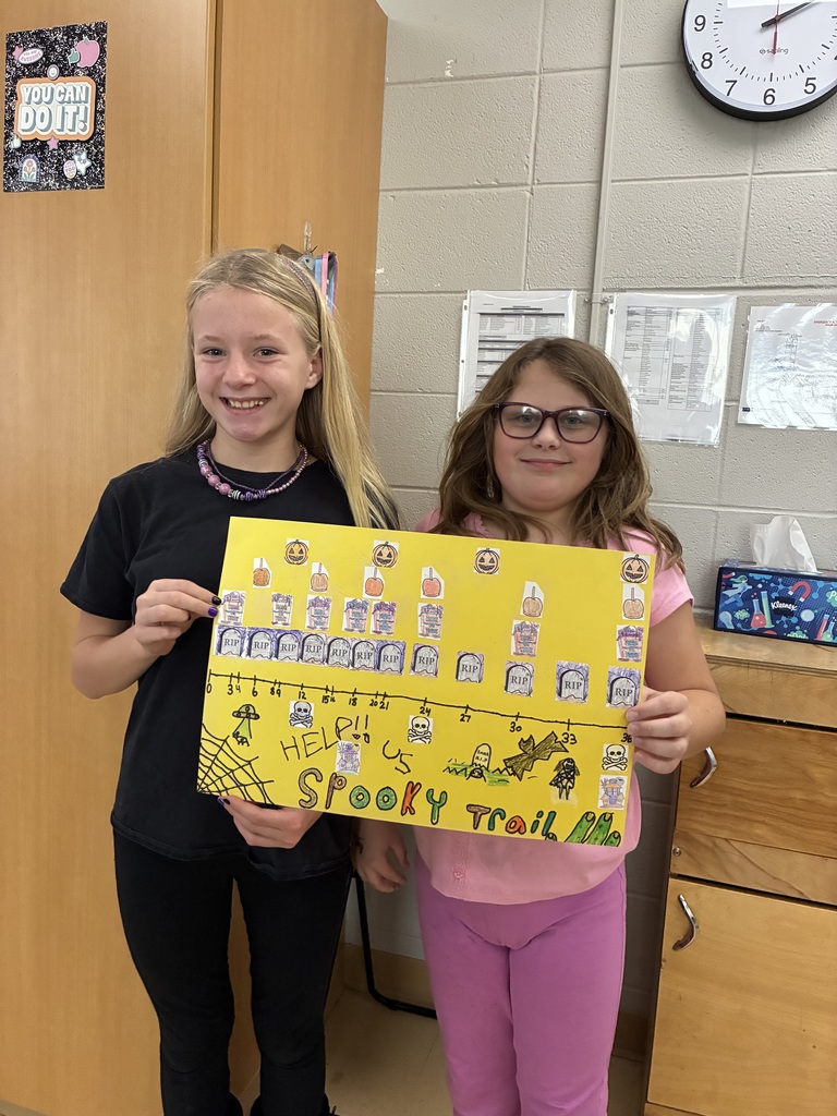 Two students holding a yellow math poster titled "Spooky Trail" featuring a Halloween-themed number line with gravestones and pumpkins.