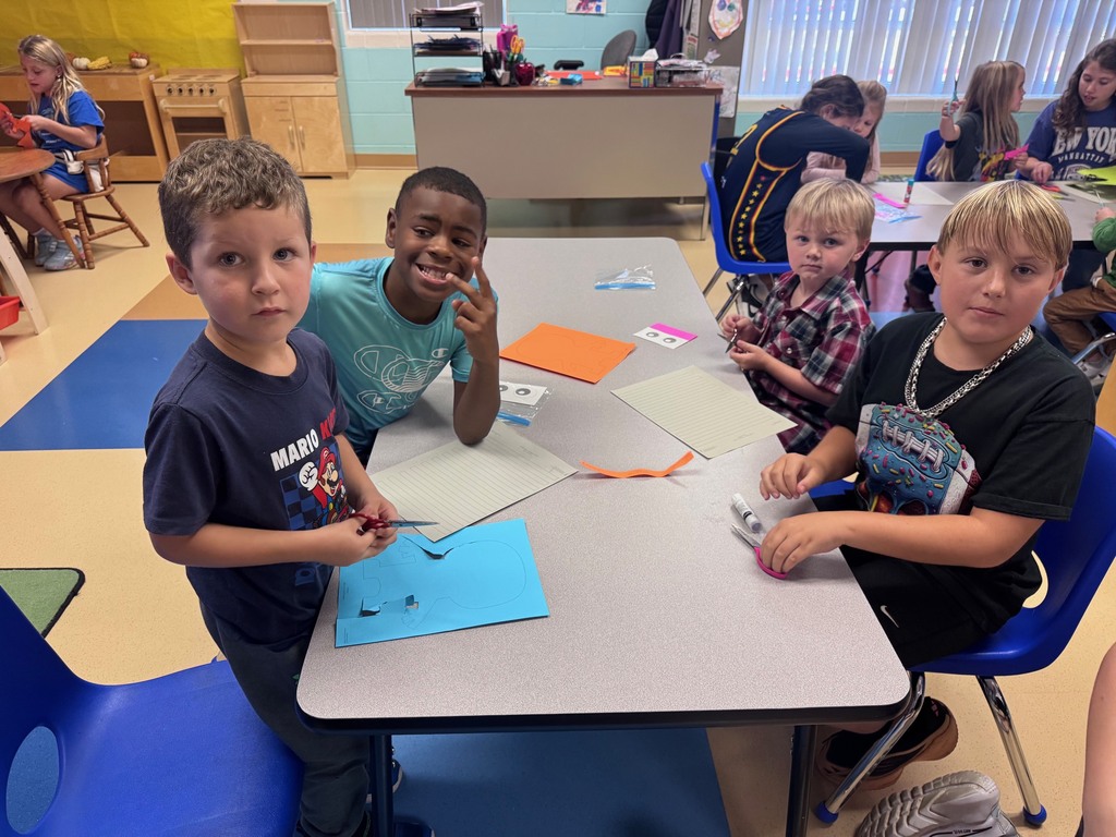 Group of students sitting around a table in a classroom, working together on arts and crafts projects.