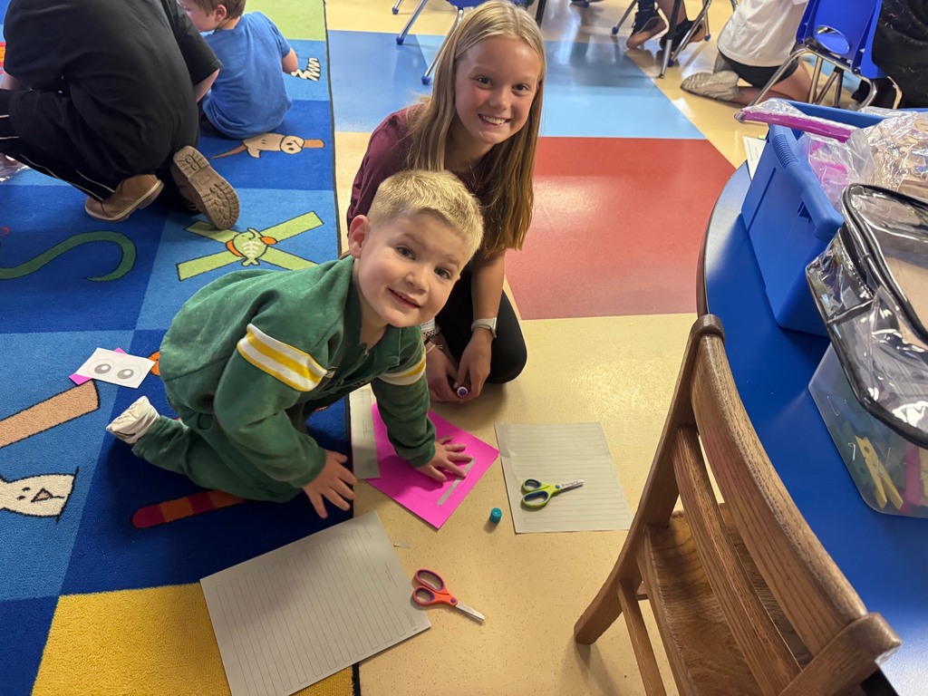 Young boy and girl smiling together while working on a craft project on the floor of a vibrant classroom.