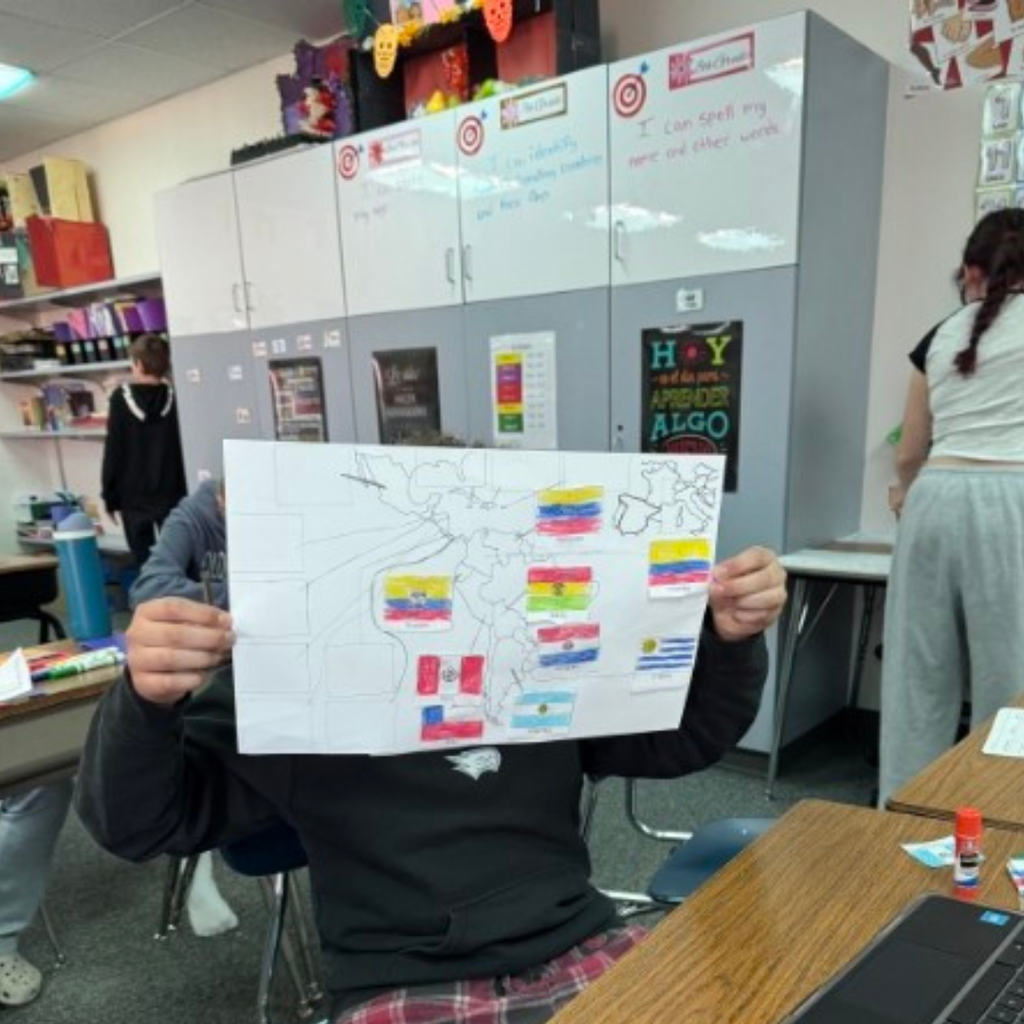 A student holding up a completed map project decorated with colorful country flag cutouts in class.