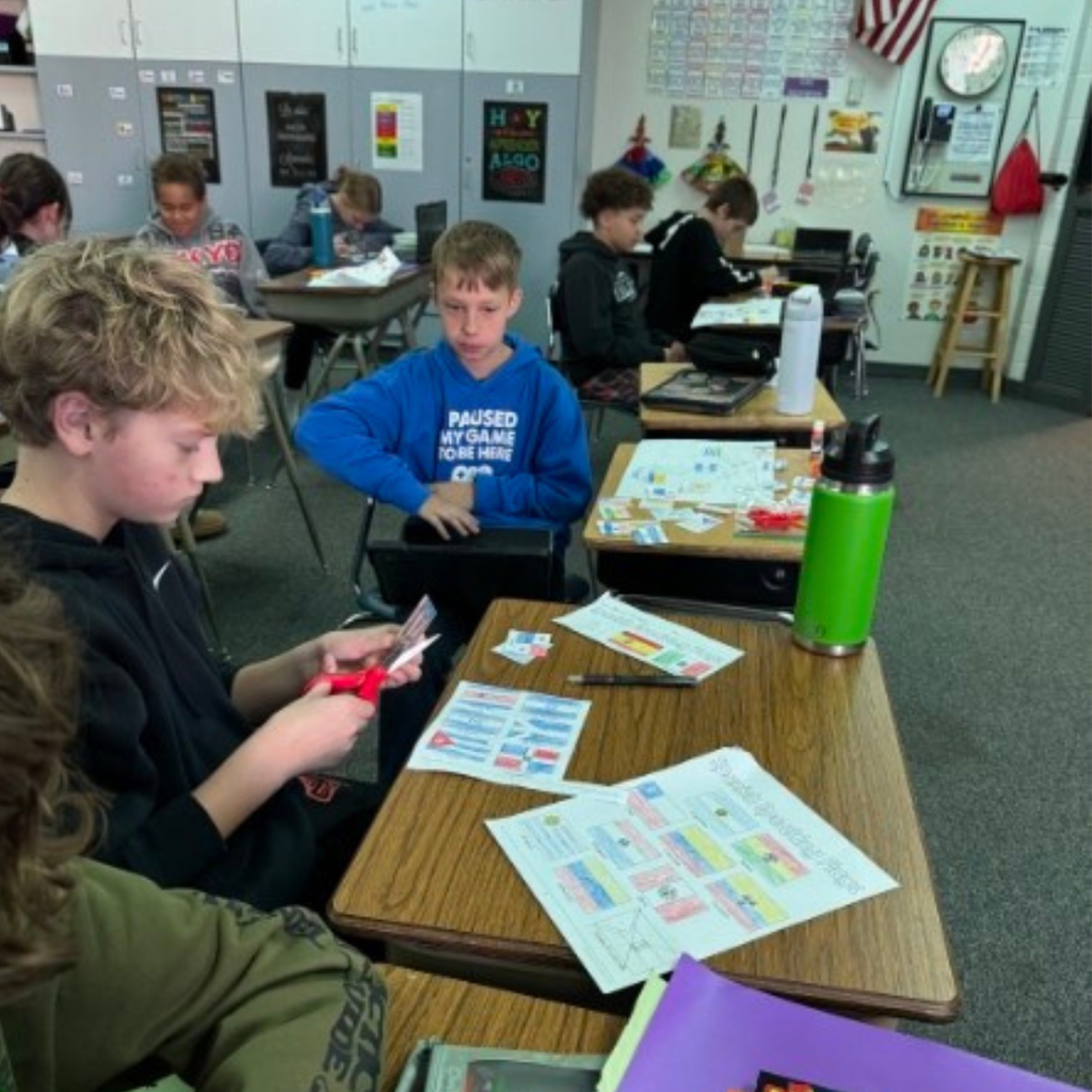 Students sitting at classroom desks cutting out printed country flag cutouts for a geography assignment.