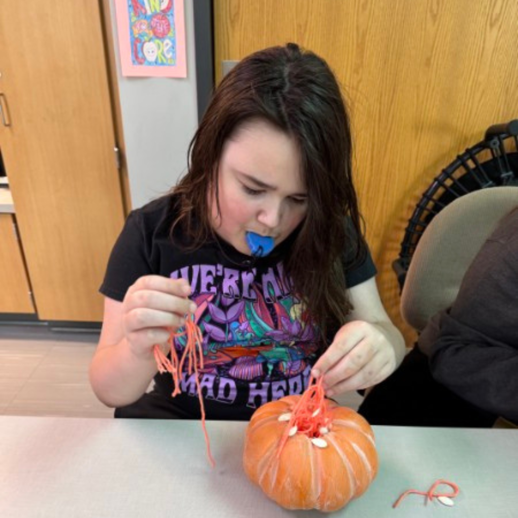A student working on a hands-on science project, pulling orange yarn pulp out of a craft pumpkin.