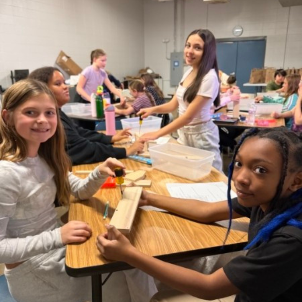 Students in a classroom using screwdrivers and tools to build projects out of wooden boards at their desks.
